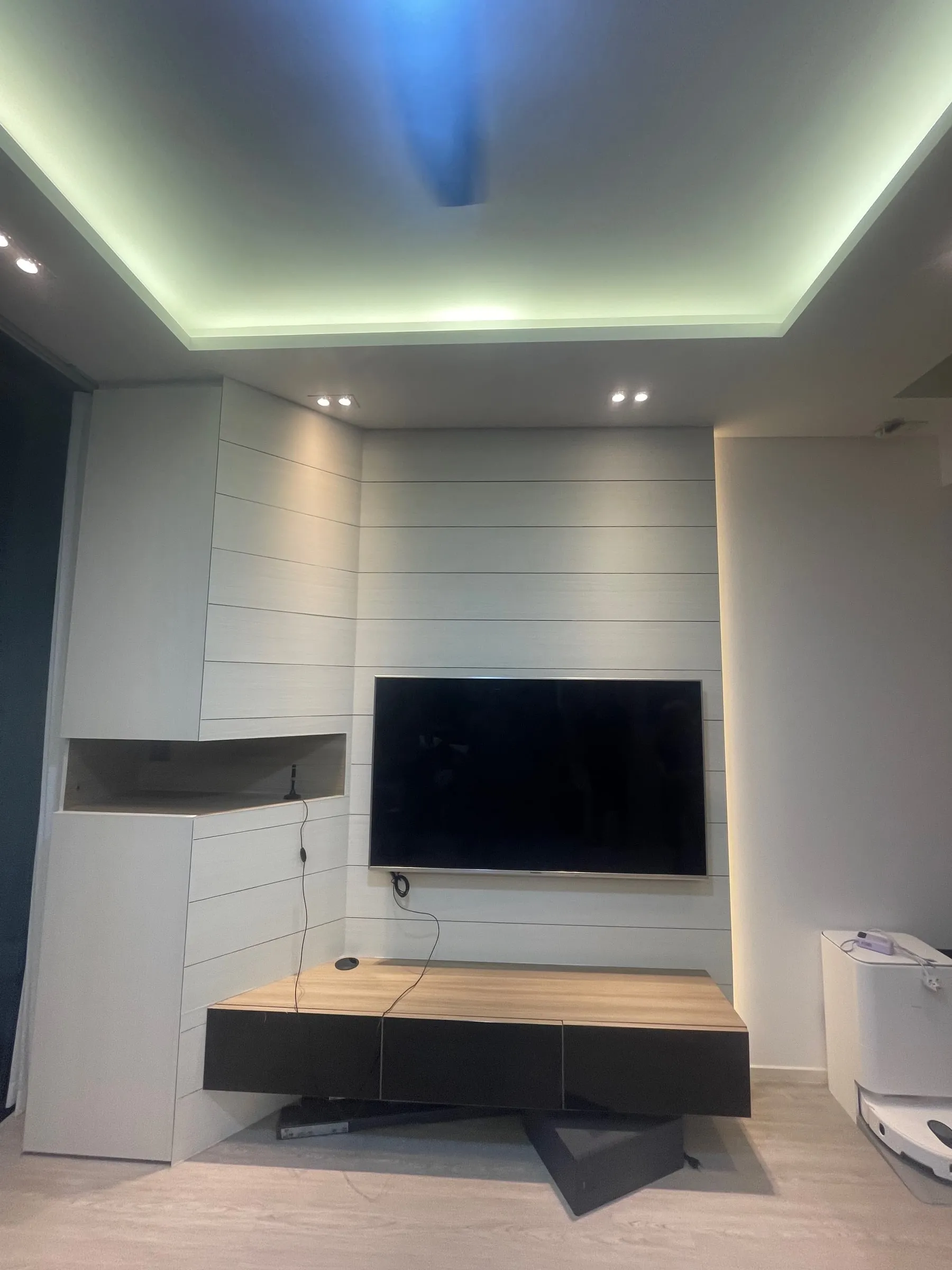 A living-room TV feature wall resurfaced in white, with cove lighting above.